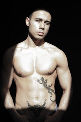 Fototapeta premium A young attractive guy with a handsome body posing under the sun in the studio.