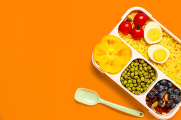 Spoon and lunchbox with tasty food on orange background