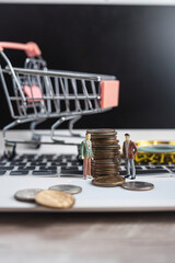 Miniature people with us coin and shopping cart on laptop for e-commerce shopping