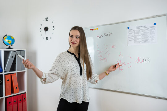 Young caucasian teacher giving lesson for english grammar near whiteboard in classroom