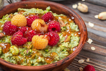 Healthy breakfast. Oatmeal matcha porridge with fresh raspberries, caramel sauce and pistachios in a bowl