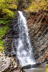 Fototapeta premium Large beautiful waterfall in autumn mountains. Wildlife. Environmental protection. Selective focus, defocus. Vertically
