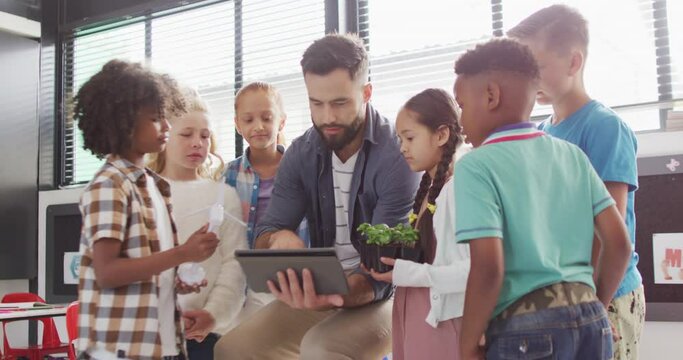 Diverse male teacher and happy schoolchildren using tablet in school classroom
