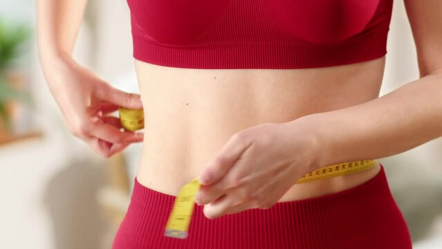 Sporty girl measuring hew waist line. Losing extra weight concept, dieting. Calorie control and fatt loss. Concept of home sport and body control