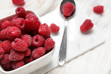 Bowl with fresh raspberry and spoon on light background, closeup