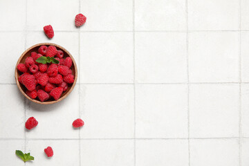 Bowl with fresh raspberry and mint on light tile background