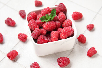 Bowl with fresh raspberry and mint on light tile background, closeup