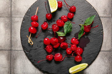 Slate board with tasty maraschino cherries on grey tile background