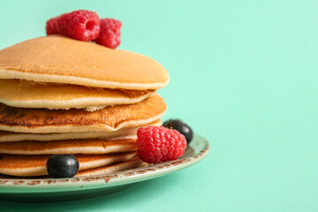 Plate of tasty pancakes with raspberries and blueberries on turquoise background