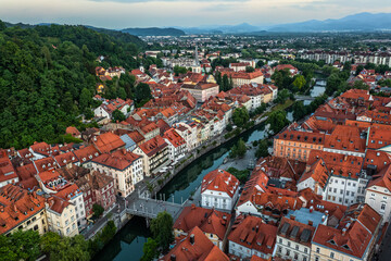 Fototapeta na wymiar Ljubljana, Slovenia - Aerial view of Ljubljana on a summer afternoon with red rooftops, Ljubljanica river, Cobblers bridge (Sustarski most) and skyline of the capital of Slovenia