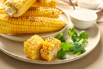 Plate with tasty grilled corn cobs and sauce on brown background