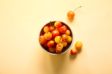Bowl with sweet yellow cherries on yellow background