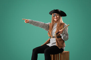 Beautiful female pirate with spyglass sitting on wooden box and pointing at something against green...