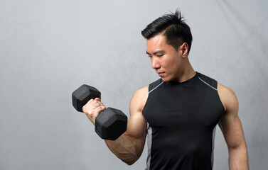 Young sports man working out with dumbbells on gray background. Closeup of a muscular young man lifting weights