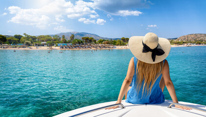 A tourist woman at summer vacation on a boat looks at the beautiful beach of Varkiza, Greece, with turquoise sea and sunshine - obrazy, fototapety, plakaty