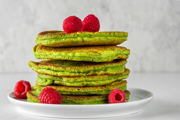 Stack of homemade pancakes with matcha tea, fresh raspberries, pistachios on white background