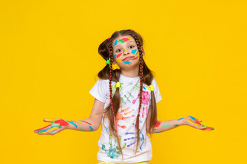 Portrait of a girl with a face painted with multicolored paints. Children's creativity. A happy child stained to the paint. Yellow isolated background.