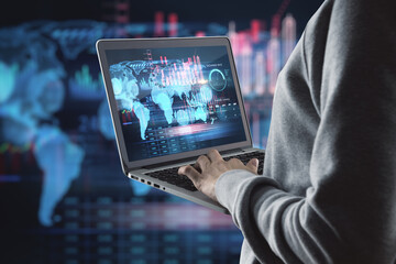 Close up of hacker hands using laptop with creative global forex chart on dark background. Concept...