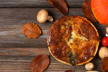 Chicken, mushroom, spinach and tomatoes pies quiche with autumn leaves on rustic wooden background. top view