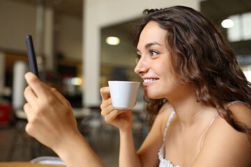 Fototapeta na wymiar Happy woman drinking coffee using cell phone in a bar