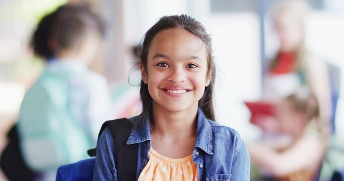 Portrait of happy biracial schoolgirl with diverse schoolchildren in background in school