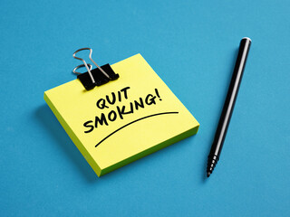 The warning message quit smoking on yellow sticky note paper with a black pen on blue background. Healthcare concept.