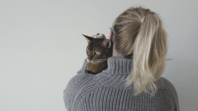 Woman with a cat. Adult girl and a cat. Love for pets. Back to the camera. Blonde. Veterinary clinic. Pet Sitter Services. Protecting pets from violence. Volunteer. Care and love.
