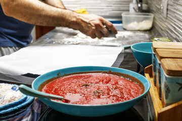 Raw pizza, preparation in traditional style. Adding tomato sauce on a pizza dough.