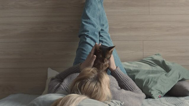 Pet Sitter. Woman with a cat on a bed in a house. Love for pets. Blonde. Veterinary clinic. Pet Sitter Services. Protecting pets from violence. Volunteer. Care and love. Home comfort and atmosphere.