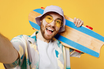Close up young man he wear blue shirt white t-shirt casual clothes doing selfie shot pov on mobile cell phone hold inahnd skateboard pennyboard isolated on plain yellow background. Lifestyle concept. © ViDi Studio