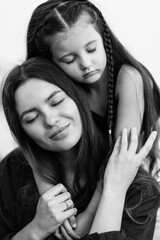 Fototapeta premium Lovely young mother with little daughter hugging with eyes closed on beach