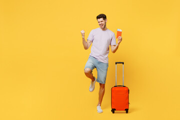 Traveler winner man wear casual clothes hold suitcase passport ticket isolated on plain yellow background studio. Tourist travel abroad in free spare time rest getaway Air flight trip journey concept