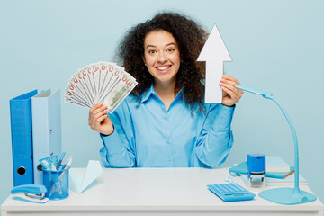 Young fun employee business woman wear casual shirt sit work at white office desk hold fan of cash...