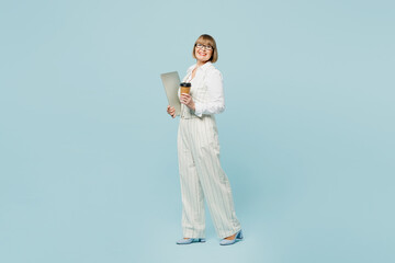 Full body employee IT business woman 50s wearing white classic suit glasses formal clothes holding closed laptop pc computer drink coffee isolated on plain blue background. Achievement career concept.