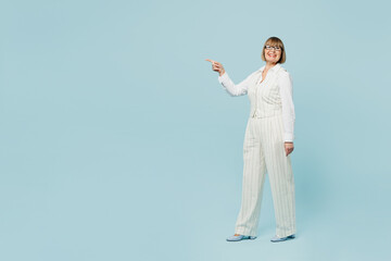 Full body fun employee business woman 50s wear white classic suit glasses formal clothes walk point index finger on workspace area isolated on plain pastel blue background. Achievement career concept