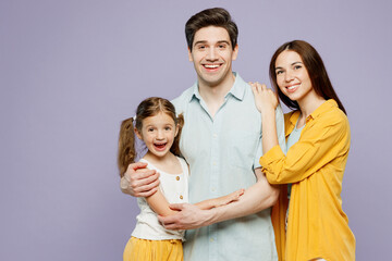 Young happy cheerful parents mom dad with child kid daughter girl 6 years old wear blue yellow casual clothes look camera hug cuddle together isolated on plain purple background. Family day concept.