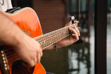 A man plays the guitar, sitting on a wooden pier near the lake.