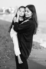 Young woman hugging her little daughter with eyes closed, while walking on beach