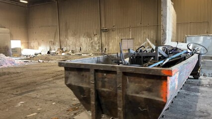 Slow pan from right to left looking at a dumpster full of scrap metal then moving into a large building