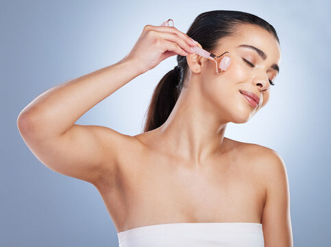 Skincare, derma roller and asian woman in studio for anti aging, cosmetic or face massage on grey background. Rose quartz, facial and female wellness model relax with microneedling, beauty or routine