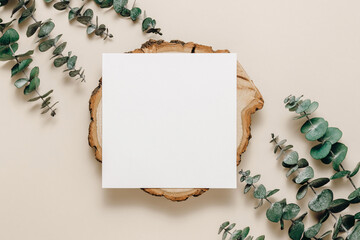 Blank paper sheet card on wooden stand with eucalyptus leaves on beige background. Aesthetic card...
