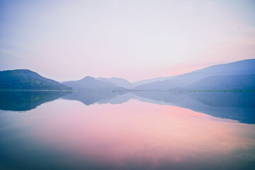 Fototapeta na wymiar A Serene Panorama of Mountain Lake Reflecting on Water with a Pink Pastel Romantic Sky at Dusk