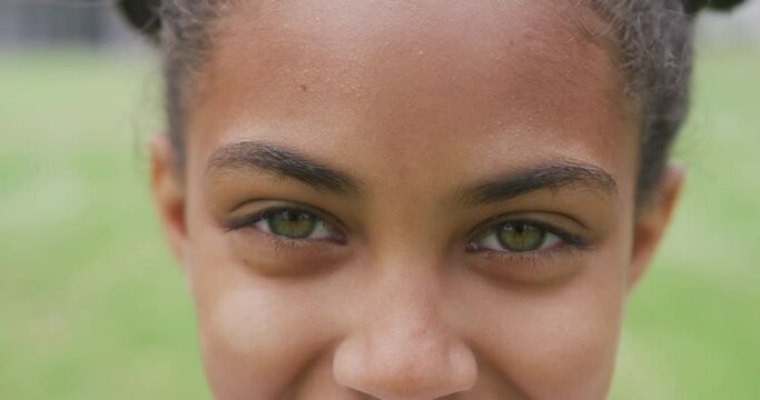 Video portrait close up of green eyes of smiling biracial schoolgirl in playing field
