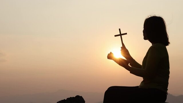 Silhouette of christianity woman catholic hand holding cross or crucifix pray to god at sunrise, person prayer in church concept of religion, spirituality, religious, believe, , faith, hope, worship.