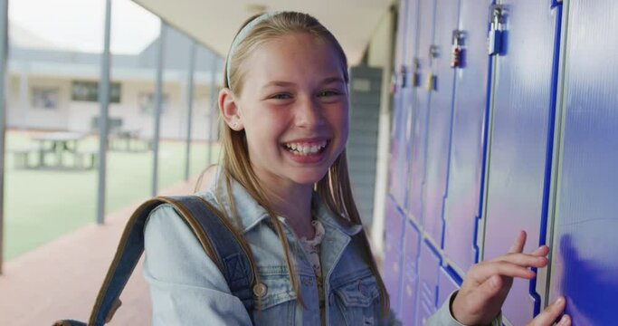 Video portrait of happy caucasian schoolgirl using locker in school corridor, copy space