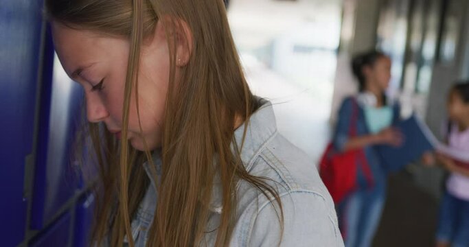 Video of sad caucasian girl crying by lockers in school corridor, copy space