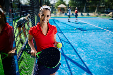 Young happy woman on paddle tennis outdoor court looking at camera.