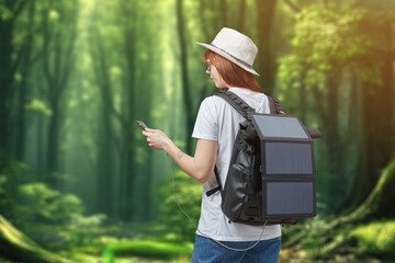 Female hiker with smartphone in hands carrying backpack with charging solar panel onforest...