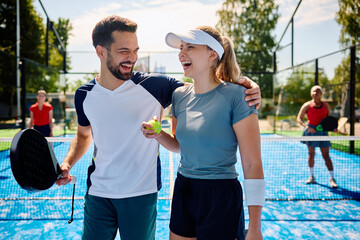 Happy paddle tennis players have fun while playing doubles on outdoor court.
