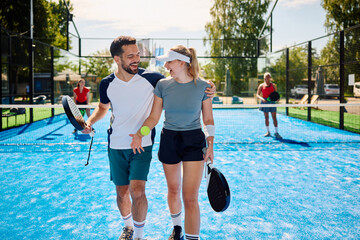 Cheerful mixed doubles partners playing paddle tennis on outdoor court.